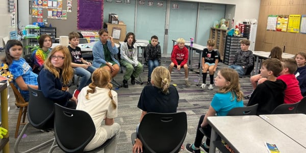 Students sit in a circle in a classroom.