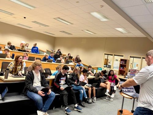 Students in a presentation hall with their laptops or tablets.