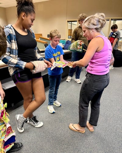 A group of students and an adult look at colorful handmade items together in a classroom.