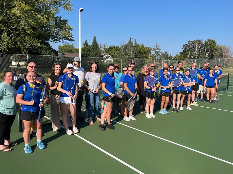 Tennis players stand on the tennis court with their parents.