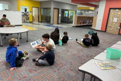 Students are sitting on the ground with books.