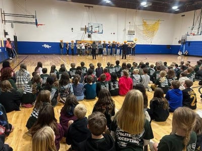 Elementary students sit in a gym during a band performance.