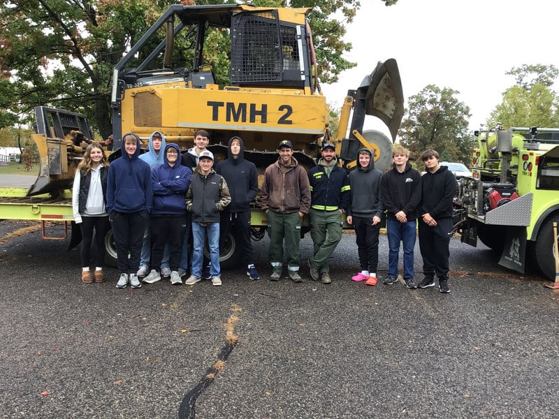 Students stand in front of a large piece of machinery.