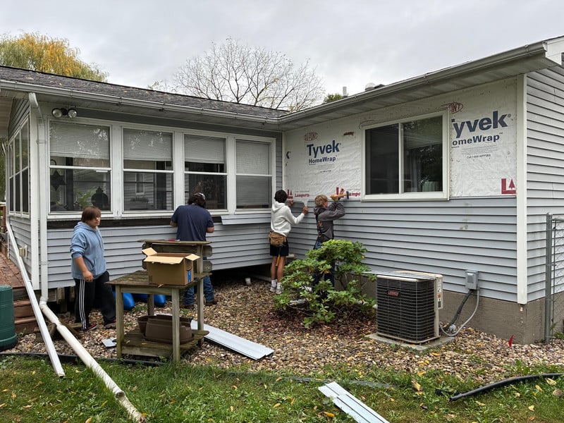 Students work on the siding of a house.