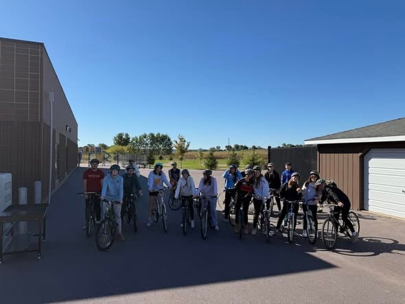 Students are on bikes in a shadow outside.