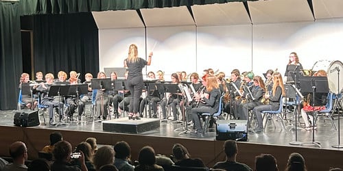A middle school band performs on stage, led by a conductor, for an audience.