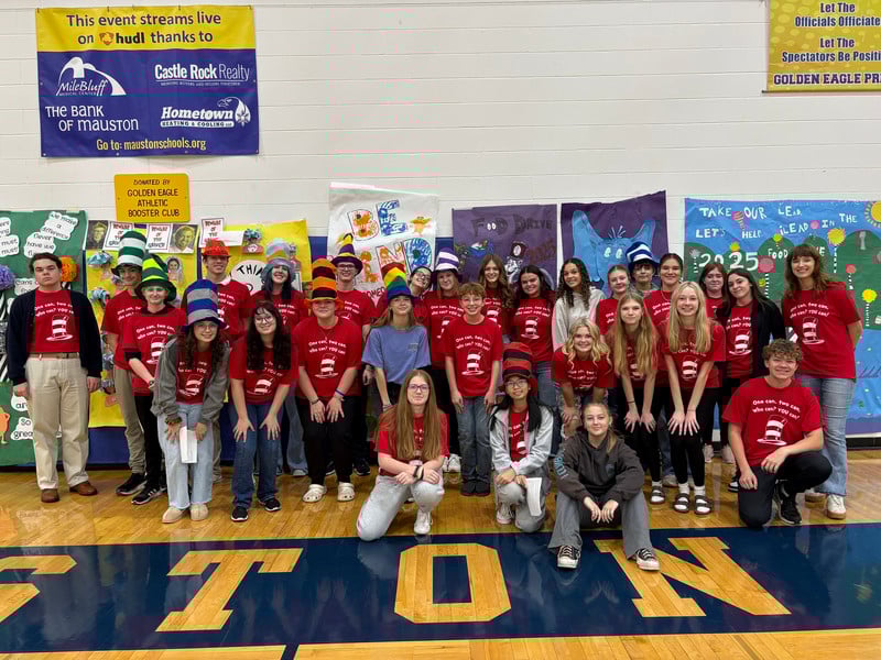 A large group of high school students pose in red shirts and colorful hats for a food drive event.