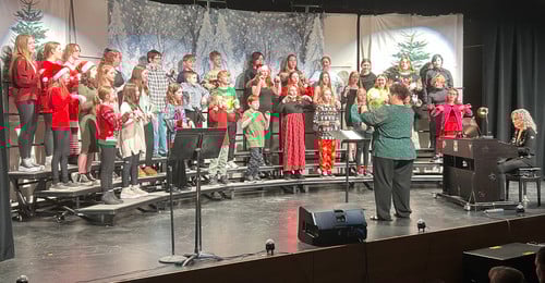 Students performing in a choir concert on a stage decorated with winter forest backdrops.