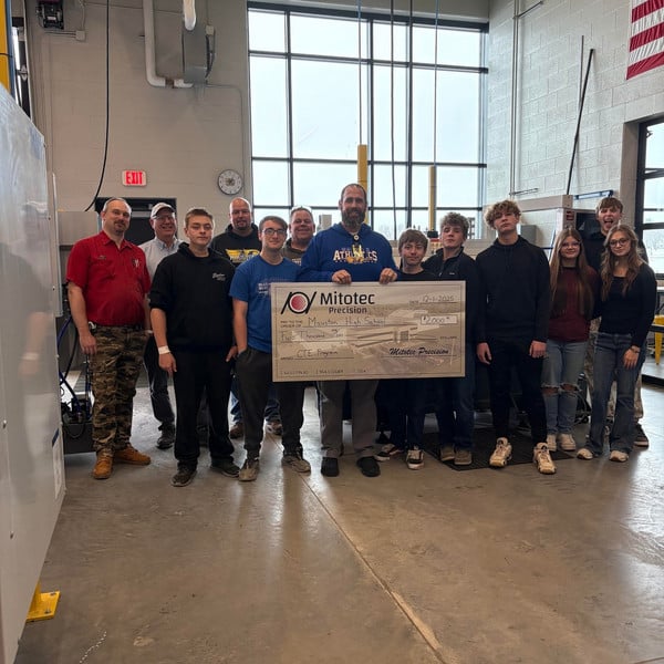 A group stands in a high school technical education department holding a large ceremonial check.