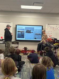 A guest speaker shows students photos of ice fishing on a digital screen in a classroom.