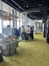 Students explore interactive exhibits at a food service science center with large windows.