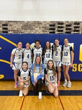 A girls' basketball team in blue jerseys poses together on the court for a team photo.