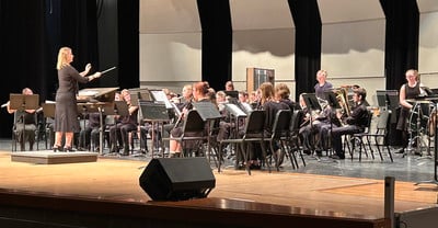 A large middle school band performs with brass, woodwind, and percussion instruments on stage.