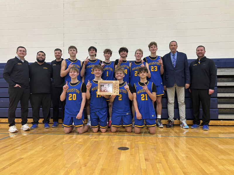 The boys' basketball team poses with their conference championship trophy on the court.