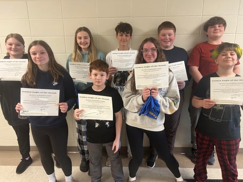 Nine students standing against a wall holding 