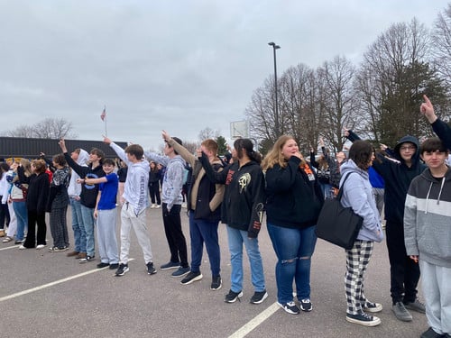 A crowd of middle school students standing outside and pointing their fingers at the sky.