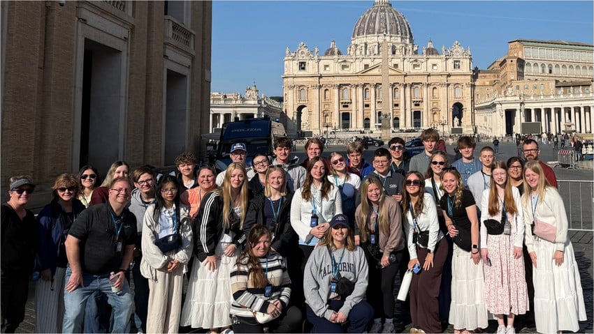 A large group of students and chaperones posing in front of St. Peter's Basilica in Rome.