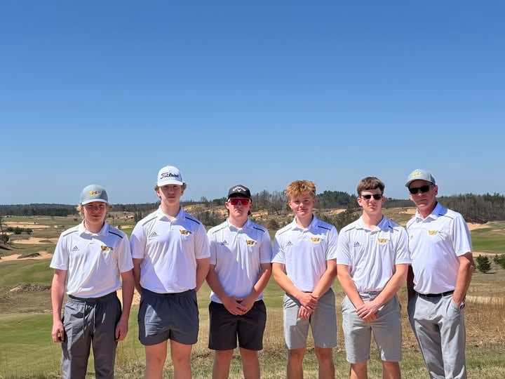 Five young men in matching white golf shirts and a coach standing on a sunny golf course.