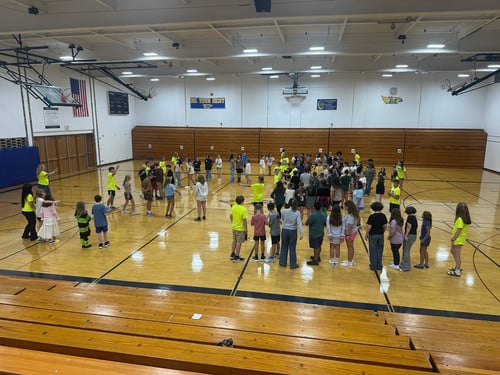Large group of students participating in an activity on a middle school gymnasium floor.